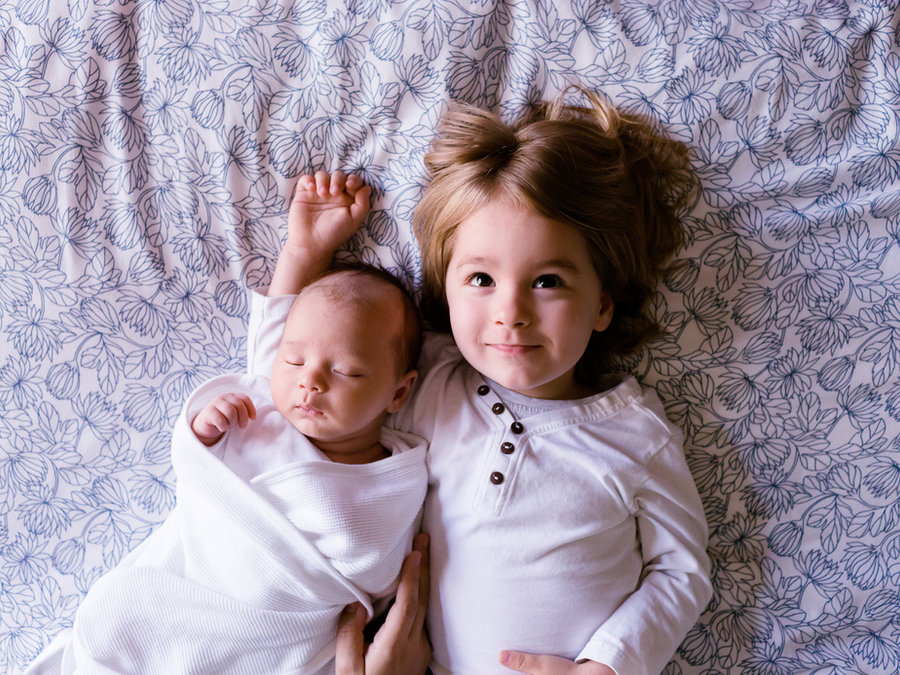 An older sibling lying beside a newborn baby