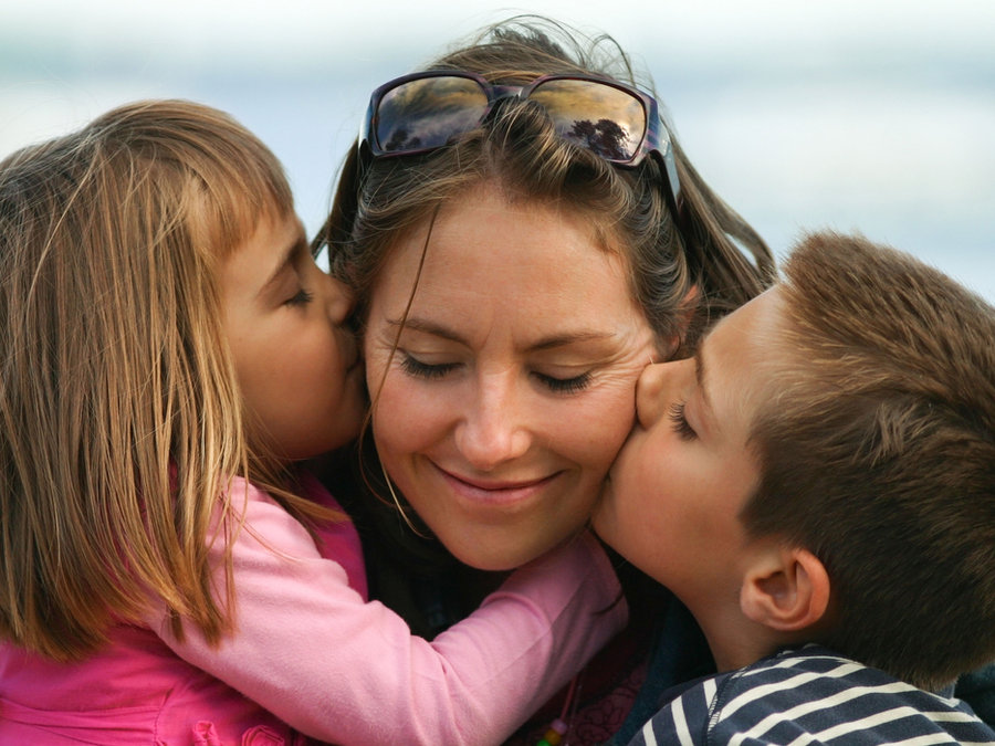 Two children kissing their mother on the cheeks